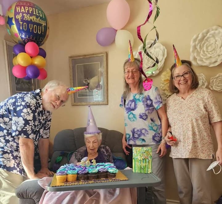 Birthday a group of people standing around a table with cupcakes and balloons